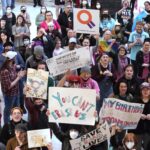 Une foule de personnes est photographiée d’en haut dans la capitale de l’État d’Oklahoma. Certains d’entre eux brandissent des pancartes faites à la main en faveur des droits des trans. Un panneau au milieu indique :