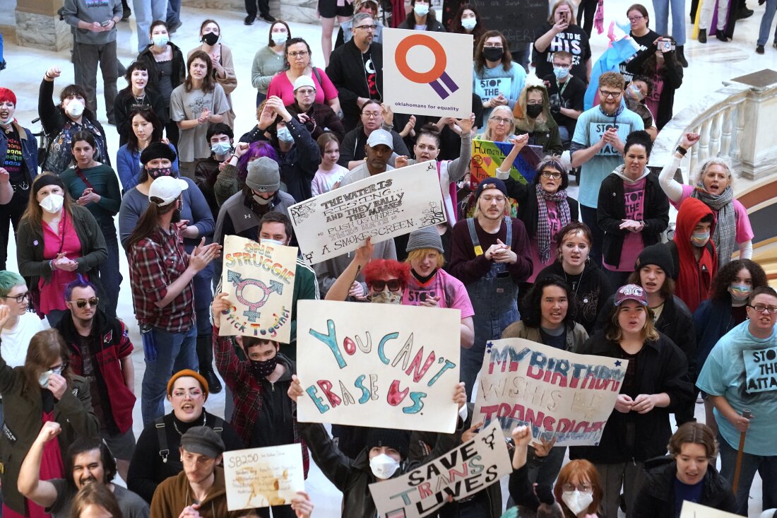 Une foule de personnes est photographiée d’en haut dans la capitale de l’État d’Oklahoma. Certains d’entre eux brandissent des pancartes faites à la main en faveur des droits des trans. Un panneau au milieu indique :