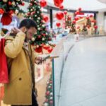 Un homme regardant son téléphone tout en faisant du shopping dans un centre commercial pendant la saison des achats de Noël.