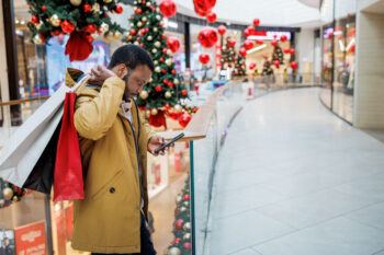 Un homme regardant son téléphone tout en faisant du shopping dans un centre commercial pendant la saison des achats de Noël.